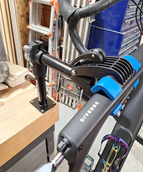 ROCKBROS bench mount with bike clamped to workbench, showing space-saving flip design